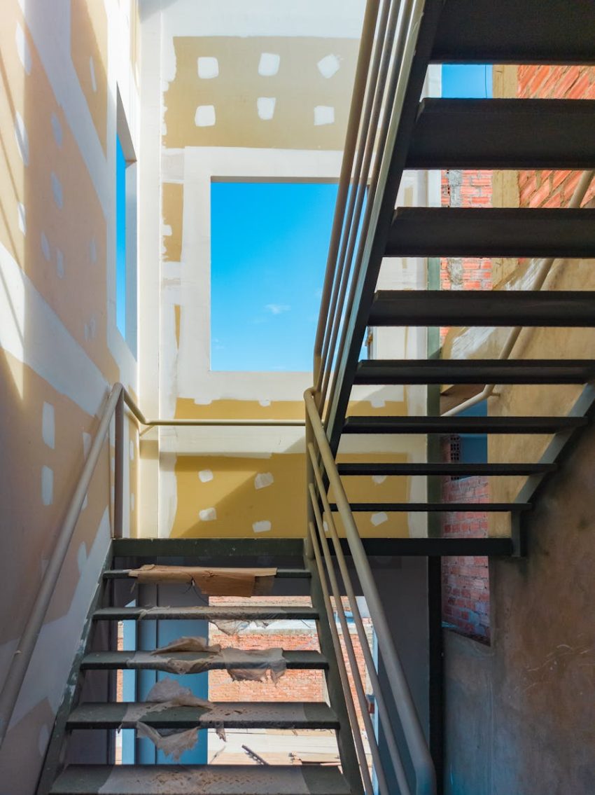 Steel staircase in a construction site with bright blue sky visible through unfinished window openings.