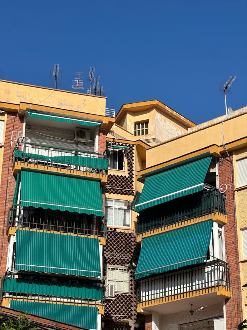 Vibrant city apartment building featuring green awnings against a clear blue sky.